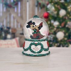 there is a snow globe with a mickey mouse in it on the table next to a christmas tree