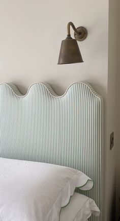 the headboard of a bed with white pillows and a lamp on top of it