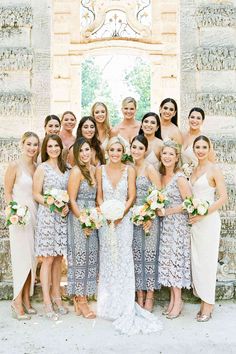 a group of women standing next to each other in front of a stone wall holding bouquets