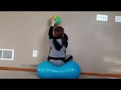 a young boy sitting on an inflatable ball and reaching up to the wall