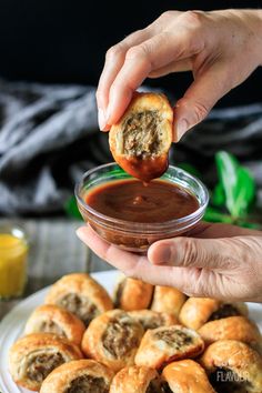 a person dipping something into a small glass bowl filled with sauce on top of pastries