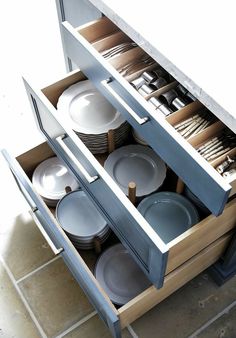 an open cabinet filled with dishes and plates on top of a tiled floor next to a counter