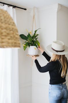 a woman is holding a potted plant in her hand and hanging it on a rope