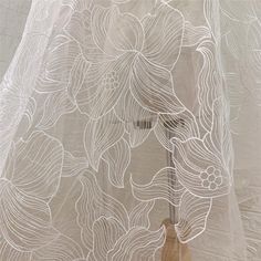 a white sheer curtain with flowers on it and a wooden stick sticking out of the bottom