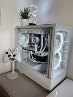 a white computer case sitting on top of a desk next to a game controller and a potted plant