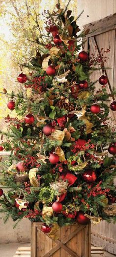 a christmas tree with red ornaments and greenery in a wooden box on the floor