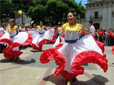 a group of women in red and white dresses dancing on the street with people watching