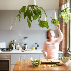 two pictures with plants hanging from the ceiling, and a woman preparing food in her kitchen