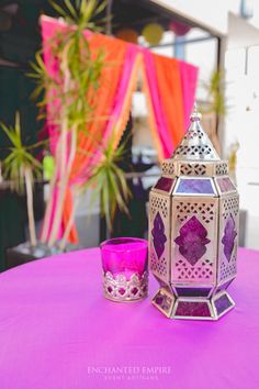 a purple table topped with a pink candle and a decorative lantern on top of it