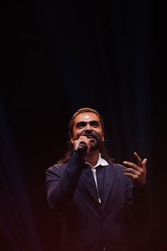 a man with long hair and beard standing in front of a microphone while wearing a suit