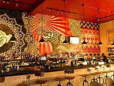 the interior of a restaurant with many tables and stools in front of a colorful wall