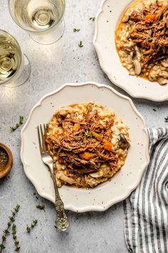 two white plates topped with food next to glasses of wine and silverware on a table