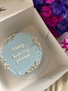 a blue birthday cake in a box with purple flowers around it and the words happy birthday princess written on top