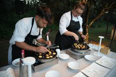 two people in aprons are preparing food on a table with white plates and silver utensils