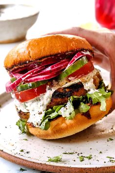 a hand holding a sandwich with meat, lettuce and tomatoes