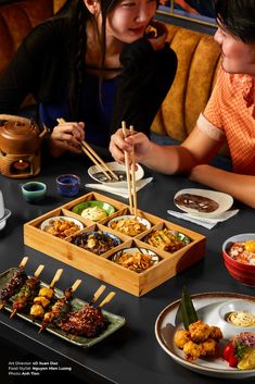 two people sitting at a table with plates of food and chopsticks in front of them