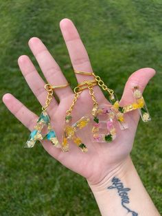 a hand holding four different colored glass beads in it's palm, with grass behind them