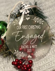 a glass ornament with the words engaged and red berries hanging from it's side