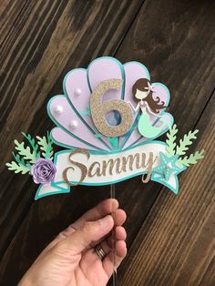 someone holding up a cake topper with the number six on it and mermaid tail