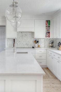 a white kitchen with marble counter tops and an island in front of the stove top