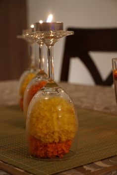 three wine glasses filled with orange and yellow flowers on a place mat next to two candles