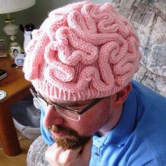 a man sitting on a couch wearing a pink knitted hat with the word brain printed on it