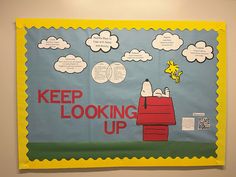 a bulletin board that says keep looking up with snoopy on top and clouds above it