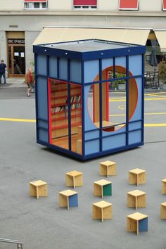 a blue and red container with shelves on the ground in front of people walking by