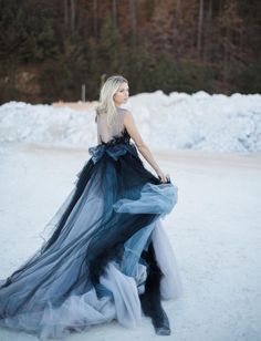 a woman is standing in the snow wearing a blue and black dress with sheer layers