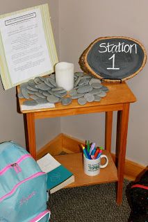 a wooden table topped with a chalk board next to a backpack and cup filled with pencils