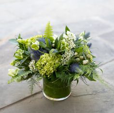 a vase filled with green and white flowers on top of a stone slabd floor