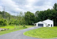 a white house sitting in the middle of a lush green field next to a forest