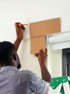 a man holding a pencil and drawing on the wall with a cardboard box in front of him