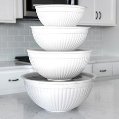 three white bowls stacked on top of each other in front of a kitchen countertop