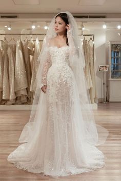 a woman standing in front of a wedding dress with long sleeves and a veil on her head