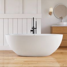 a large white bathtub sitting on top of a wooden floor next to a mirror