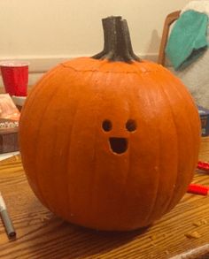 a pumpkin with a face drawn on it sitting on a table next to markers and pens