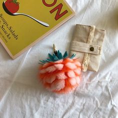 an orange and blue pom - pom on top of a white bed next to a book