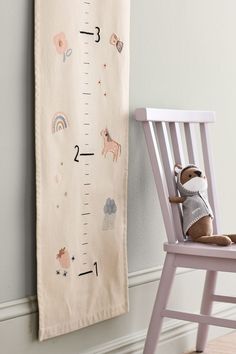 a teddy bear is sitting on a chair next to a growth chart wall hanging from the wall