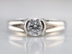 a white gold ring with a round cut diamond in the center on a reflective surface