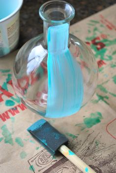 a glass vase with a blue handle next to a paintbrush on top of a piece of paper