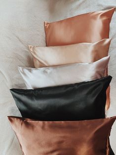 four different colored pillows sitting on top of a white bed sheet with black and gold trim