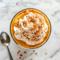 a cup filled with whipped cream on top of a white table next to a spoon