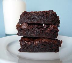 two chocolate brownies stacked on top of each other next to a glass of milk