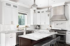 a white kitchen with marble counter tops and stainless steel appliances, along with two bar stools