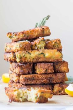 a stack of food sitting on top of a white plate next to lemon wedges