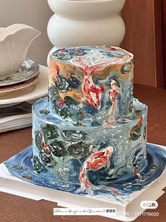 a three tiered cake with koi fish painted on the top and bottom layer