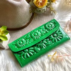 two green leather wallets sitting on top of a white fur covered floor next to flowers