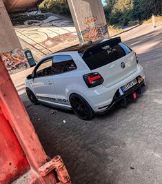 the rear end of a white car parked under an overpass in a parking lot