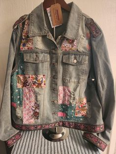 an old jean jacket with patches and flowers on the front, hanging from a clothes rack